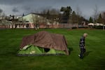 FILE: With Fruitdale Elementary School in the background, a homeless person walks near a tent in Fruitdale Park, Saturday, March 23, 2024, in Grants Pass, Ore. The rural city of Grants Pass in southern Oregon has become the unlikely face of the nation's homelessness crisis as its case over anti-camping laws goes to the U.S. Supreme Court. The case has broad implications for cities, including whether they can fine or jail people for camping in public.