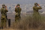 Israeli soldiers uses binoculars to look at damaged buildings in the Gaza Strip, from southern Israel, Wednesday, Aug. 13, 2025.