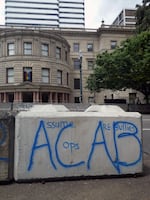 Anti-police graffiti covers barricades that line both sides of the street outside Portland City Hall. A rainbow flag inside the building's windows acknowledges June as LGBT Pride Month.