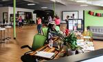 A Human Solutions intern sits at the front desk of the Rosewood Initiative. Behind her, community members dance in a free Zumba class offered through Portland Parks and Recreation. 