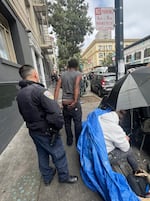 San Francisco police officers detain a man for "illegal lodging" under a tarp and umbrella in the Tenderloin.