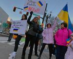 Four people hold protest signs and wave Ukrainian flags. One sign reads, "Ukraine deserves to stay free." Another reads, "Stop Putin NOW!!"