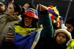 A woman standing among a crowd of people wears the Venezuelan flag draped across her chest and shoulders as they all celebrate outside the Metropolitan Detention Center in Brooklyn, New York.