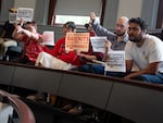 Democratic Socialists of America lobbyist Jordan Lewis, center right, gestures a thumbs down with others upstairs in the council chambers.