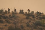A firefighting crew hikes up a hillside while clearing brush  just inside the Warm Springs Reservation, on the edge of the Bench and Beachcomber Fires, seen from Madras, Ore., on July 27, 2026.