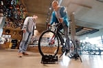 FILE- In this Nov. 13, 2018, photo Vitalii Myroshnychenko, right, test rides a bike atop a stand as Denis Rybalchenko looks on in REI Co-op's flagship store in Seattle.