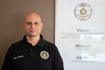 A man wears a black polo shirt with the logo of the Bend Police Department on one side of his chest and the words "Chief M. Krantz" on the other.