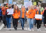 A crowd of students, many in orange shirts that say "March for Oure Lives" on them, march in a protest for tougher gun restrictions.