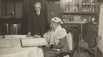 A photo of Abigail Scott Duniway, seated, holding a pen, signing a voter registry.