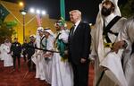 In this 2017 photo, taken at a welcome ceremony in Riyadh, Saudi Arabia, President Trump is wearing a dark suit and holding a sword while flanked by men wearing traditional white robes who are also holding swords. 