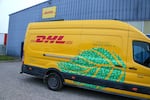 A yellow and red DHL delivery vehicle with a green leaf pattern on it is seen in front of a warehouse in Valence, France, in December 2024. 