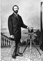 In this image, circa 1860s, photographer Peter Britt stands next to one of his early cameras. His right hand holds a lens cap, which was used as a shutter.