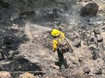 A firefighter sprays water from hose onto smoldering hillside during mop-up operations at the Tunnel 5 Fire area on July 6, 2023.