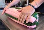 Two white-skinned hands roll a batch of pink and green taffy on a metal table.
