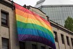 A man affixes a giant rainbow flag to the front of a building in Portland's Old Town/China Town neighborhood.