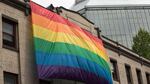 A man affixes a giant rainbow flag to the front of a building in Portland's Old Town/China Town neighborhood.