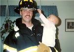 A family photo of Doug Miller in his firefighter uniform carrying Elizabeth, when she was a baby.