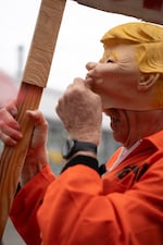 A protester wears a Trump mask in an orange prison jumpsuit costume.