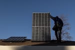 A contractor carries a solar panel on the roof of a home.