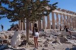 A woman drinks water in front of the ancient Parthenon Temple during a hot, windy day at Acropolis hill , in Athens, Tuesday, July 16, 2024. Much of Greece was also sweltering in a heat wave due to last until the end of the week, with temperatures in some areas forecast to reach 42 degrees Celsius (over 107 degrees Fahrenheit).
