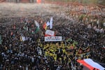 A religious procession moves through dense crowds of pilgrims in the area between the two holy shrines in Karbala, carrying flags, banners and portraits of religious figures during the Arbaeen commemoration.