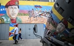 People walk past a mural depicting former Venezuelan president Hugo Chavez alongside Venezuelan independence heroes in Caracas on Dec.17, 2025.