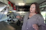 A woman in a tan jacket talks and gestures as she stands in the gleaming interior of a renovated food cart.