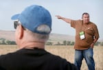 Pambrun, wearing a Brown Carhart shirt and a buzzcut, points toward the hazy horizon of the Blue Mountains. A gray-haired man in sunglasses and a baseball cap follows looks to where Pambrun is pointing.