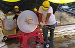 People wearing yellow hard hats crank great lengths of hose onto a spindle