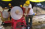 People wearing yellow hard hats crank great lengths of hose onto a spindle