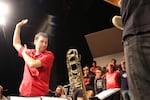 A man in a red shirt conducts a high school choir.