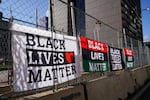 Banners arrayed along a fence all read "Black Lives Matter" in different fonts and colors