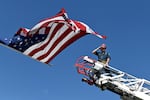 A captain with the Clifton Fire Protection District salutes the passing procession carrying the bodies of three firefighters killed while fighting the Snyder Fire in Grand Junction, Colo., on June 28. He is at the top of a ladder on a fire truck and an American flag waves above him.