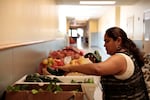 In this undated photo provided by the Oregon Food Bank, volunteer and food bank recipient Maria A. Rojas-Mendoza picks up vegetables at the Free Food Market run by Oregon Food Bank at Earl Boyles Elementary School. Last year, 2.5 million people visited free food sites in Oregon and southwest Washington last year, a 31% increase from the year before.