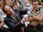 FILE - In this June 15, 1995 file photo, O.J. Simpson, left, grimaces as he tries on one of the leather gloves prosecutors say he wore the night his ex-wife Nicole Brown Simpson and Ron Goldman were murdered in a Los Angeles courtroom. Simpson, the decorated football superstar and Hollywood actor who was acquitted of charges he killed his former wife and her friend but later found liable in a separate civil trial, has died. He was 76.
