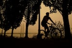 A person rides a bike along the Willamette River as smoke from wildfires partially obscures the Tilikum Crossing Bridge, Saturday, Sept. 12, 2020, in Portland, Ore.