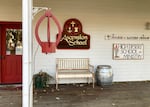 A white building with a red door features a sign that states "Ascension School" to the right of the door.