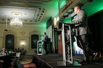 Nick Brown and Pete Serrano debate on a stage in a ball room with deep green lighting.