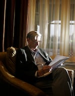 A person sits in an armchair near a curtain and reads documents.