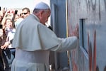 Pope Francis holds his hand against Israel's separation barrier in the Occupied West Bank town of Bethlehem while onlookers take pictures.