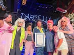 The Darcelle cast posing with the Guinness World Record certificate. From left: Alexis Campbell Starr, BinKyee Bellflower, Bebe Jay, Poison Waters, Summer Lynne Seasons, Mr. Mitchell, and Cassie Nova.