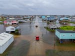 In this aerial image, vehicles drive through flooded neighborhoods on in Surfside Beach, Texas on Wednesday.