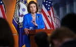 Nancy Pelosi wears a blue blazer and speaks at a podium in front of the U.S. flag.