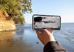 A foreground image on a cell phone of paddlers in dugout canoes with a beach in the background.