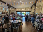 Pictured are several tables filled with seated individuals. Mini Pride flags banner across the room. A rainbow balloon arch can be seen near the entrance. Southern Oregon Coast Pride were the organizers for a drag bingo event last year at Front Street Provisioners in Coos Bay.