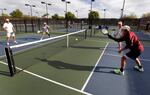 Four people on an outdoor court play a game of pickleball.