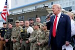 President Trump holds a mic and stands next to National Guard members and federal officers during a visit to the U.S. Park Police Anacostia Operations Facility.