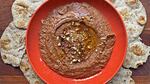 A red bowl filled with muhammara, surrounded by flatbread.