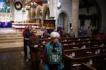 A woman with short white hair leads an interfaith meditation practice while standing next to pews in a church.