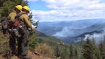 Firefighters read a map while smoke fills a valley below them.